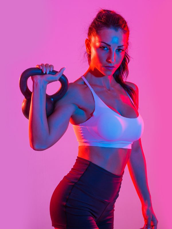Girl wearing white sports bra and black cycling while holding a round dumbbell