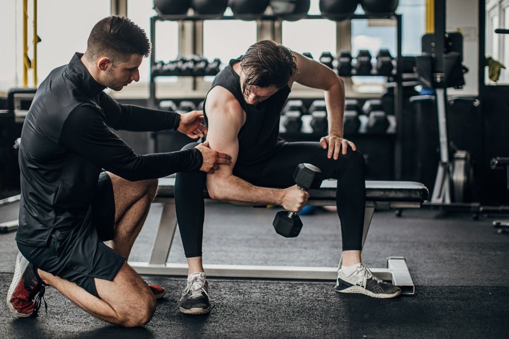 Gym trainer assisting a man with dumbbell for personal training