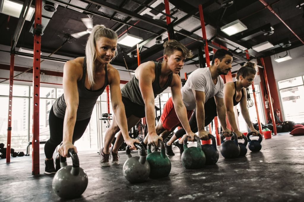 Four people exercising in gym with round dumbbell